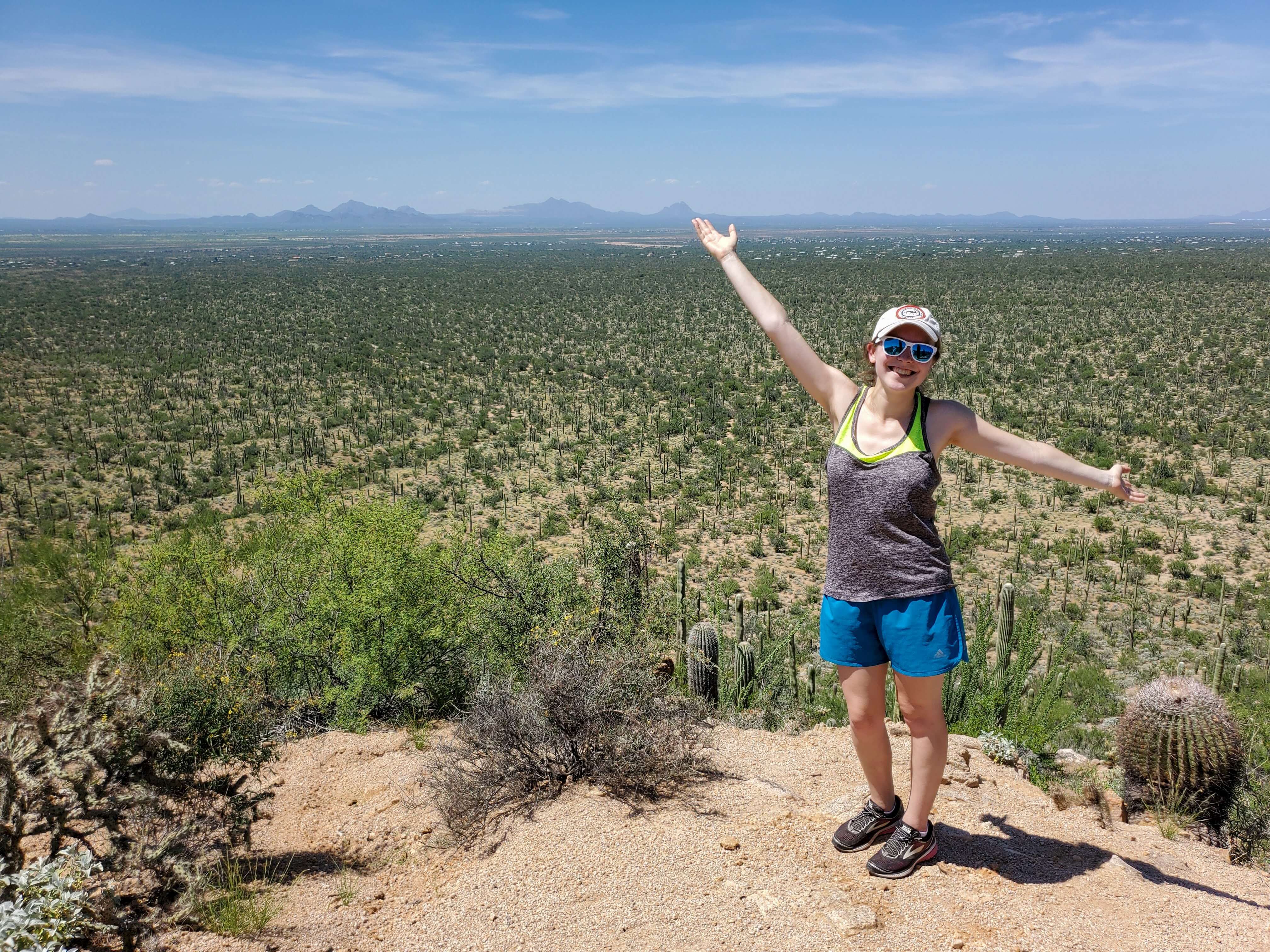 A female hiker posing in front of a valley of saguaro as soon from Valley View Overlook in Saguaro National Park