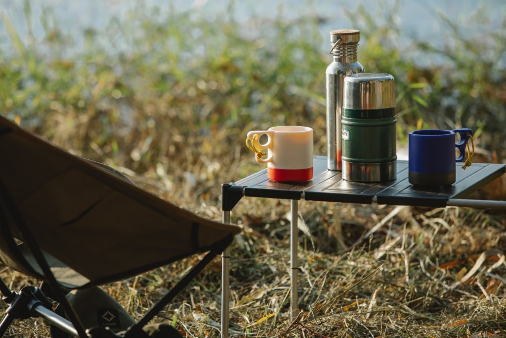 A small table outdoors with reusable dishes on it including a mug, thermos, and water bottle