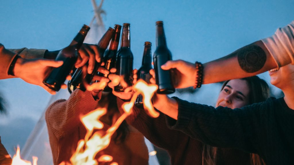 A group of friends toasting their drinks next to a campfire