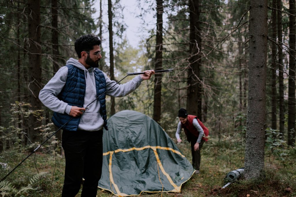 Man holding camping tent pole in front of green tent