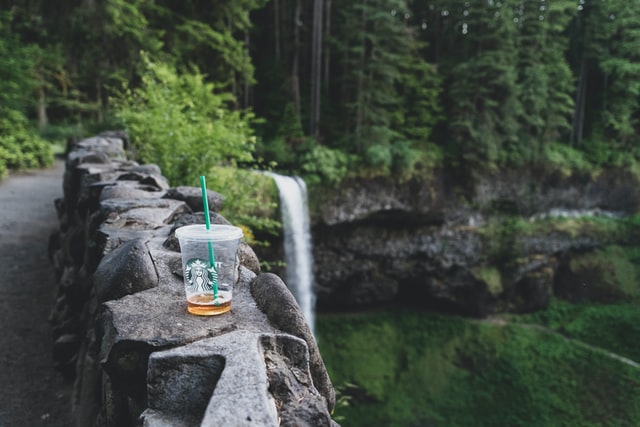 A clear coffee cup sitting on a ledge in front of a waterfall