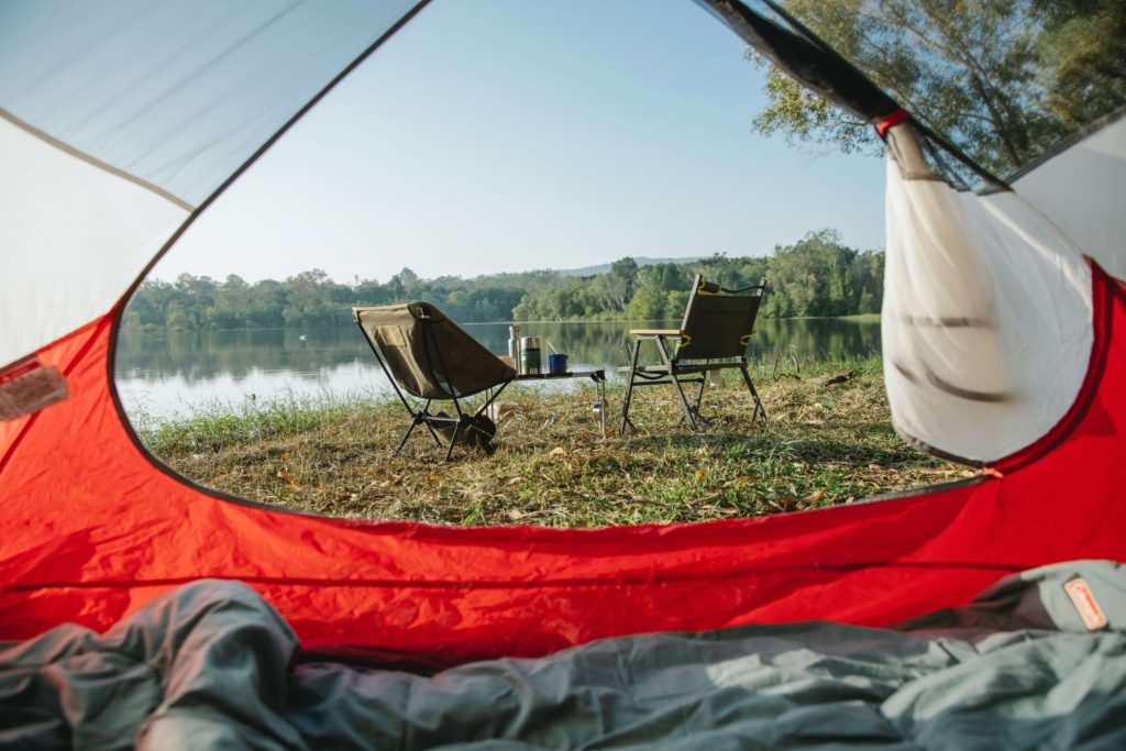 An open tent looking out at two camping chairs in front of a lake