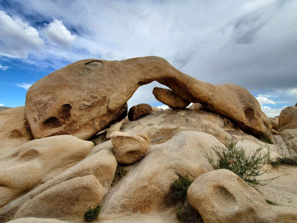 An arch-shaped rock under a cloudy sky in the desert