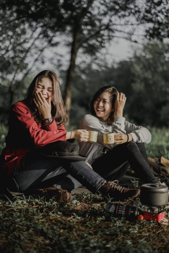 Two women sitting on the ground laughing while holding mugs