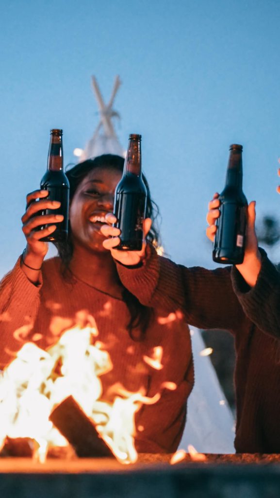 A woman with her friends holding bottles at a campfire
