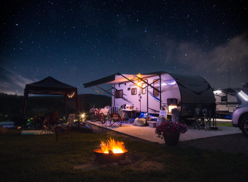 A camper next to a fire pit and a pop up tent on a starry night