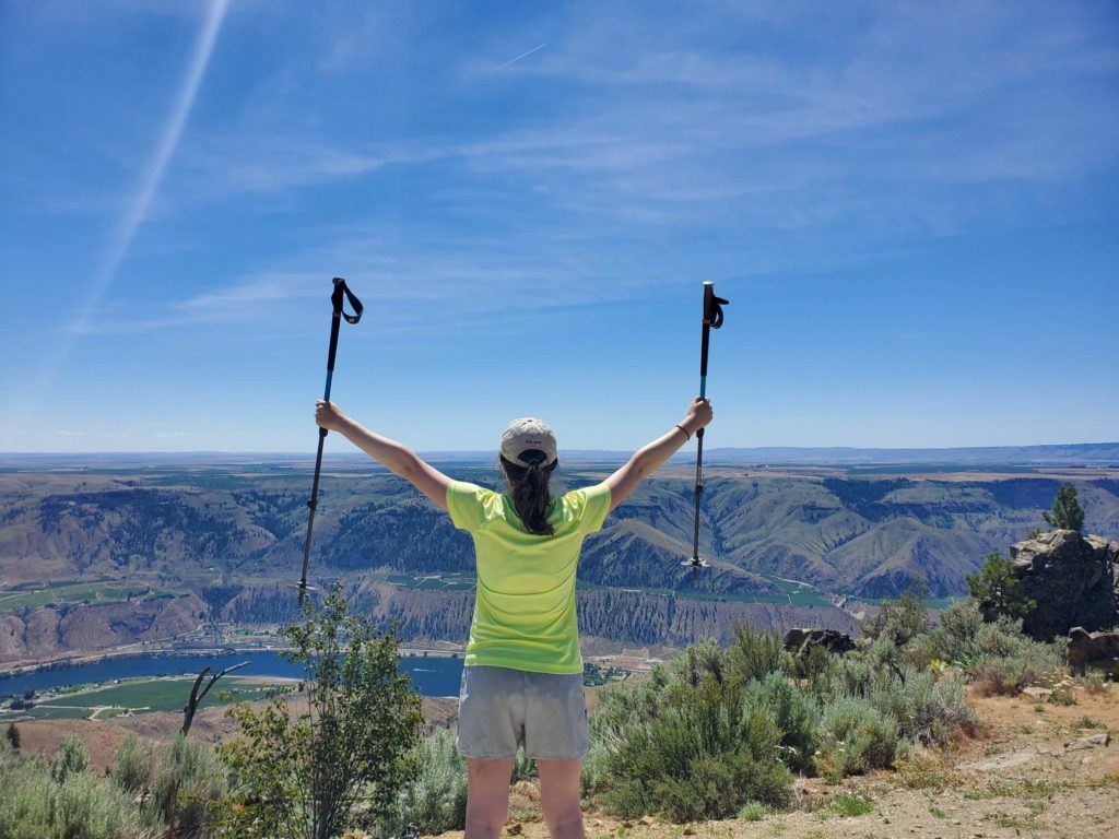 A hiker holds trekking poles in the air victoriously