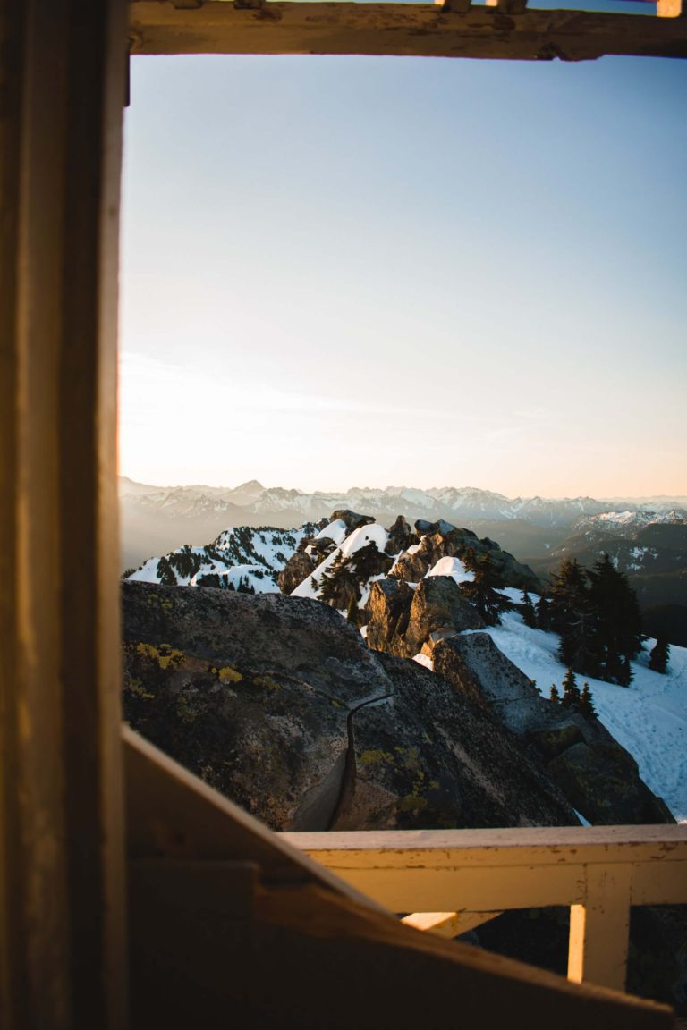 Snowy, jagged brown mountains framed by the lookout tower on Mount Pilchuck in Washington