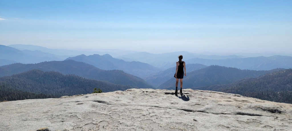A hiker standing on a rock looks out at a mountain range