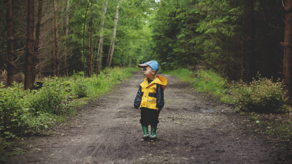 A child wearing rain gear stands on a trail