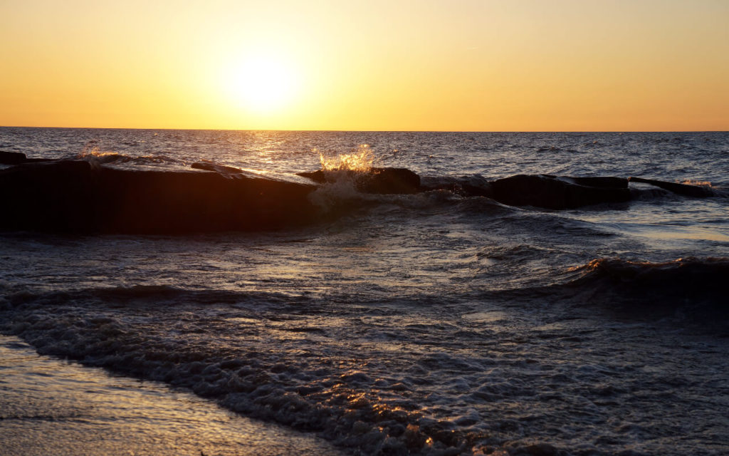 A wave crashes under an orange sunset