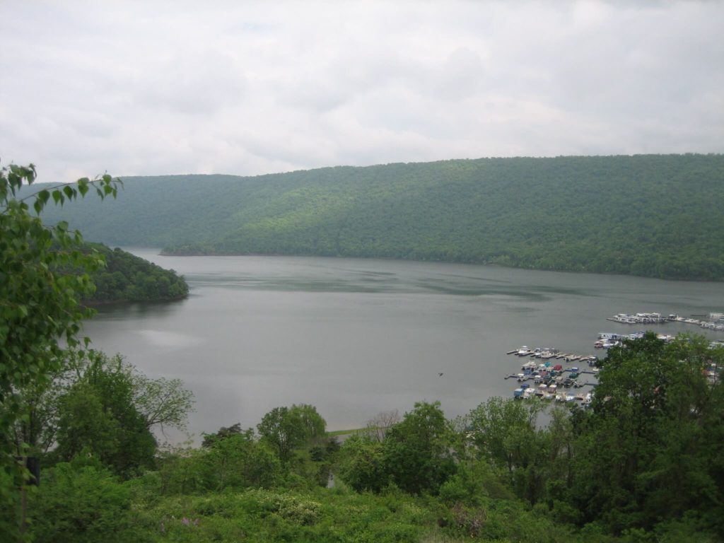 A lake surrounded by green hills under a cloudy sky