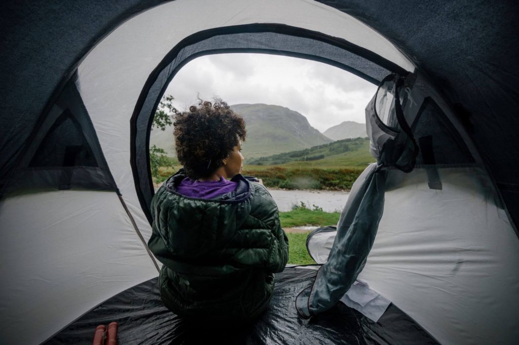 A woman sitting in a tent looks out at the rain