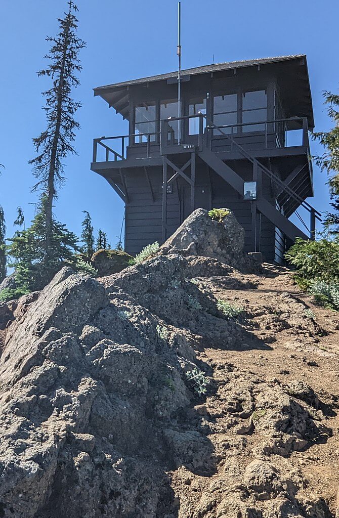 A brown fire tower stands at the top of a rocky hill