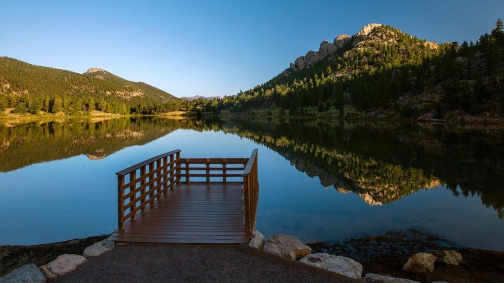 A dock extends into the calm blue water of Lily Lake, which is reflecting the mountains that surround it