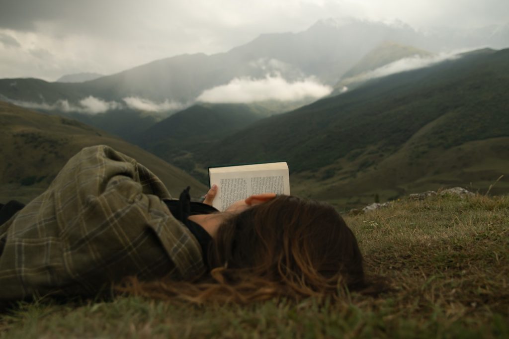 A woman reads a book lying down in front of mountains
