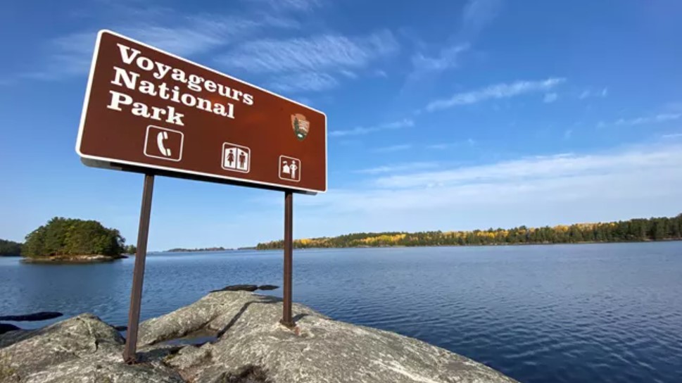 A brown sign for Voyageurs National Park stands in front of a lake